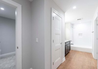 Bright modern bathroom at end of hallway with white walls, white tub/shower, and dark wood vanity countertop