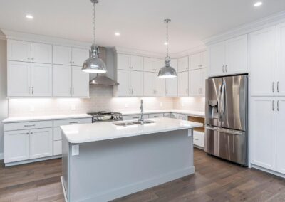 Bright, modern kitchen with white cabinets, a gray island, and stainless steel appliances under pendant lighting.