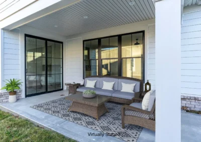 Covered patio with gray cushioned wicker sofa, chairs, and a coffee table on a patterned outdoor rug, in front of glass doors.