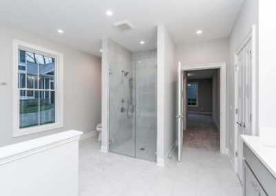 Bright modern bathroom with a glass-enclosed marble shower, toilet, and a window letting in natural light.