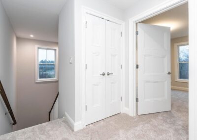 Upper-floor hallway with beige carpet, white paneled doors, and an open doorway to a room with a window.