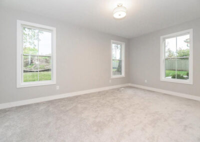 Empty living room with three large windows, light gray walls, white trim, and beige carpet awaiting furnishings.