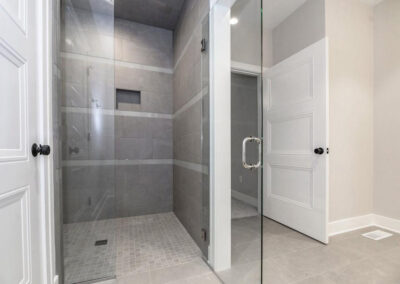 Glass-walled walk-in shower with gray tile walls, small square floor tiles, and a recessed niche