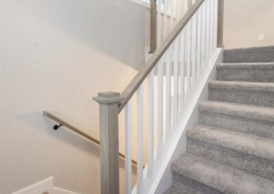 Interior staircase with gray carpeted steps, white balusters, and gray wooden handrails beside a wall of windows letting in natural light