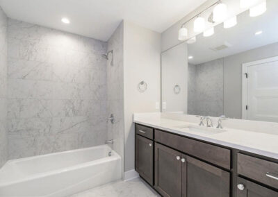 Modern bathroom with marble-tile shower and tub, dark wood vanity, and large mirror with a six-bulb light fixture above it.