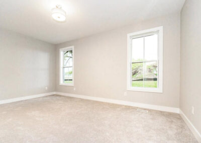 Empty light-gray room with two white-framed windows and beige carpet.
