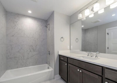 Modern bathroom with a marble-tiled shower and white tub on the left, and a dark wood vanity with a wide countertop on the right.