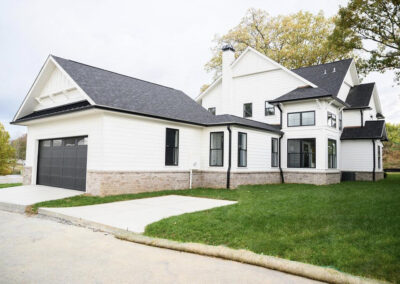 Front view of a white two-story house with a dark roof, attached two-car garage, brick foundation, and a green lawn.