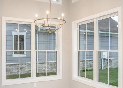 Bright dining corner with large white-framed windows, light wood flooring, and a gold circular chandelier. Informative: shows a well-lit interior space with a modern chandelier and multiple windows.