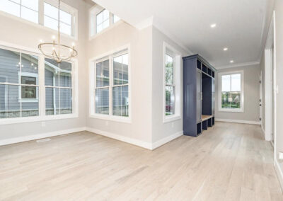 Bright open living area with tall windows, a circular chandelier, light wood floors, and navy storage cubbies along the wall.